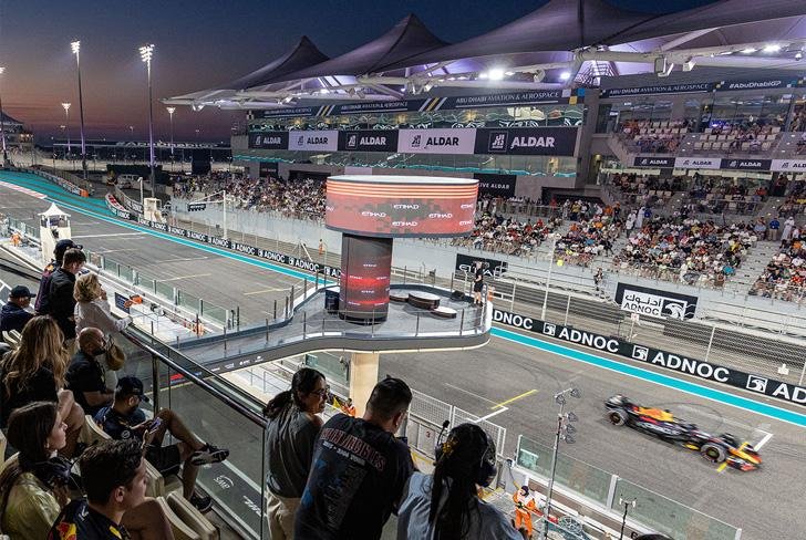 Spectators watching a Formula 1 car pass the main grandstand at the Abu Dhabi Grand Prix at dusk