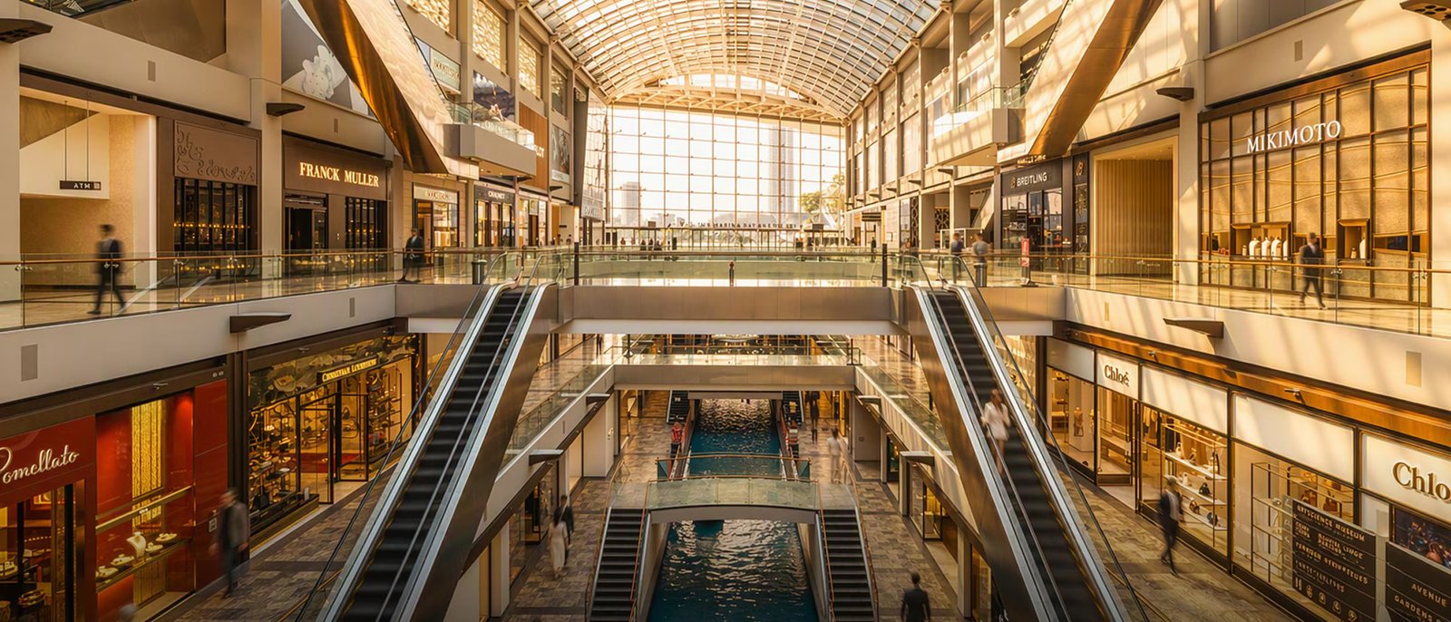 The interior of a luxury retail mall, escalators running between floors of brand storefronts